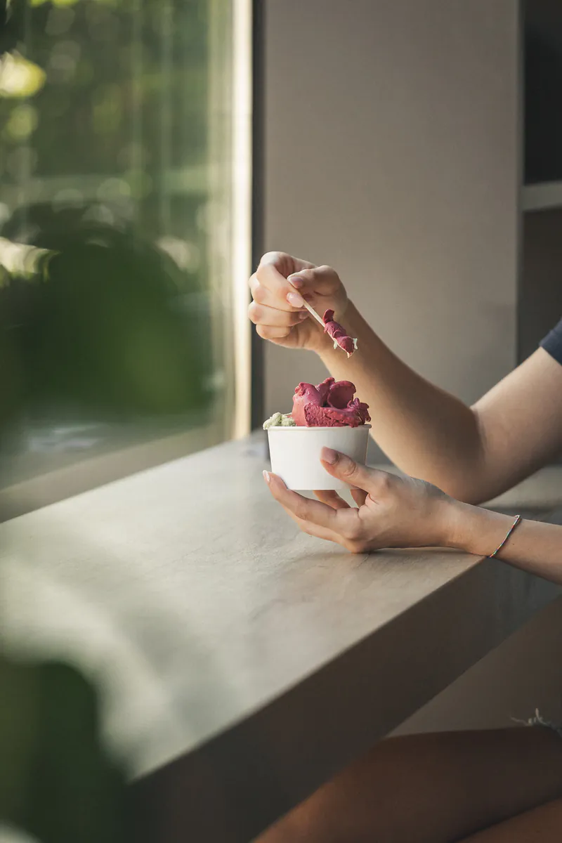 Coppetta di gelato artigianale ai frutti di bosco gustata accanto a una finestra luminosa.