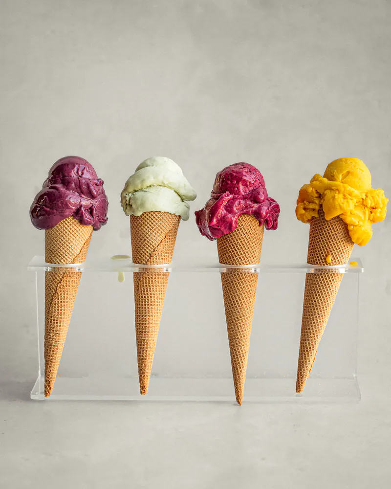 Quattro coni di gelato artigianale Saimon in colori diversi, allineati su un espositore trasparente.