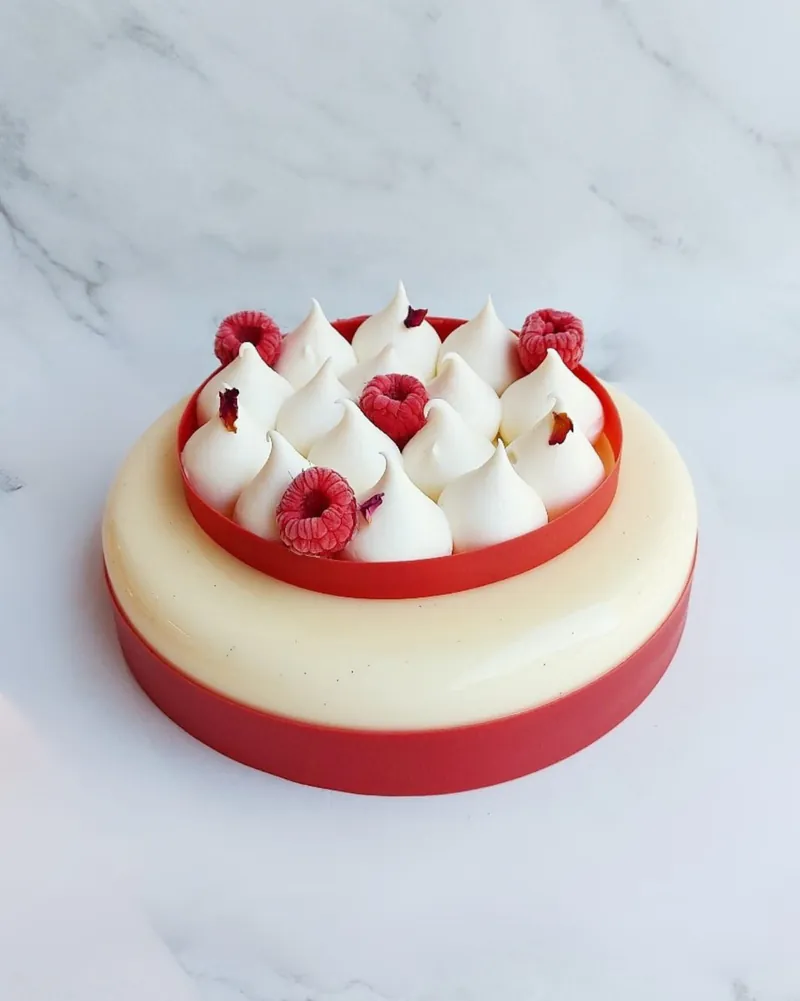 Torta semifreddo Aurora, con meringhe a ciuffo, lamponi freschi e petali di rosa in superficie.