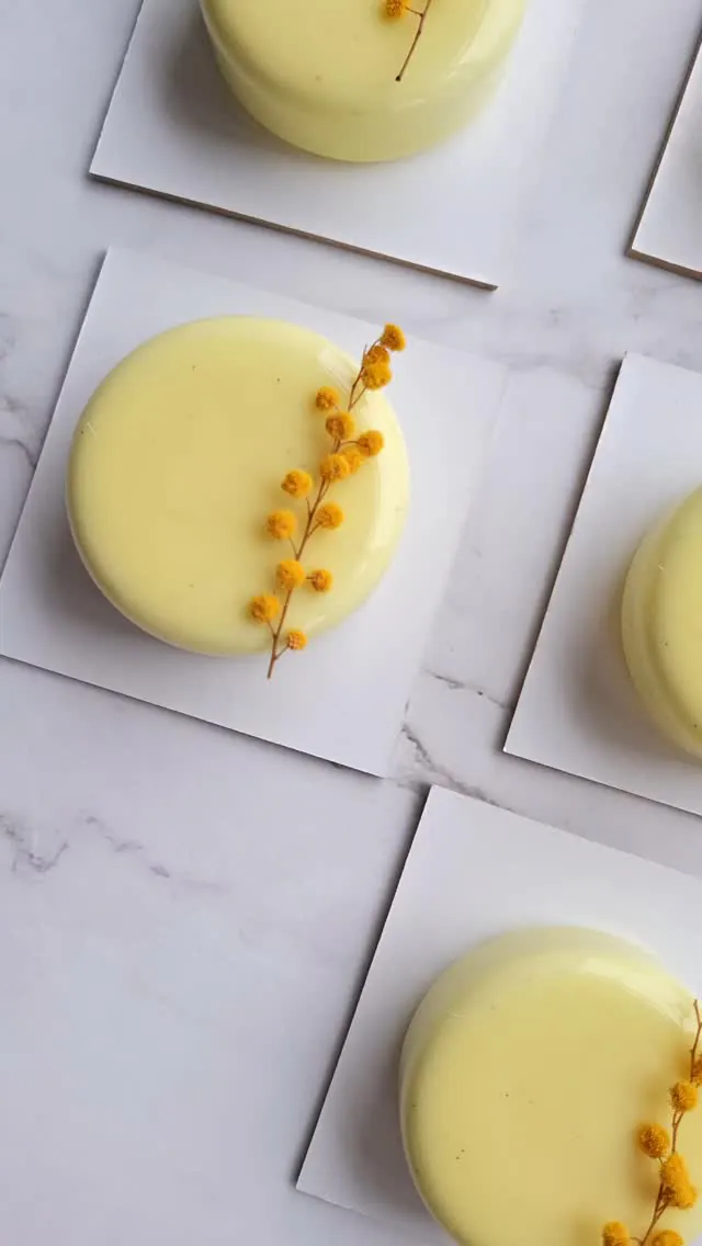 Monoporzioni semifreddo con glassa giallo tenue e un rametto di mimosa.