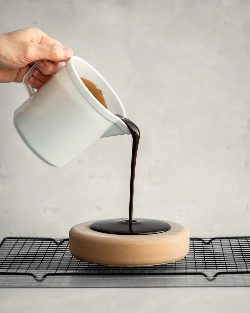 Glassa al cioccolato versata da una lattiera su un semifreddo appoggiato alla griglia.