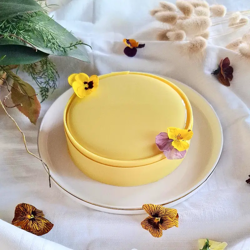 Torta semifreddo Isla, con glassa gialla al mango, una fascia di cioccolato e viole del pensiero in superficie.