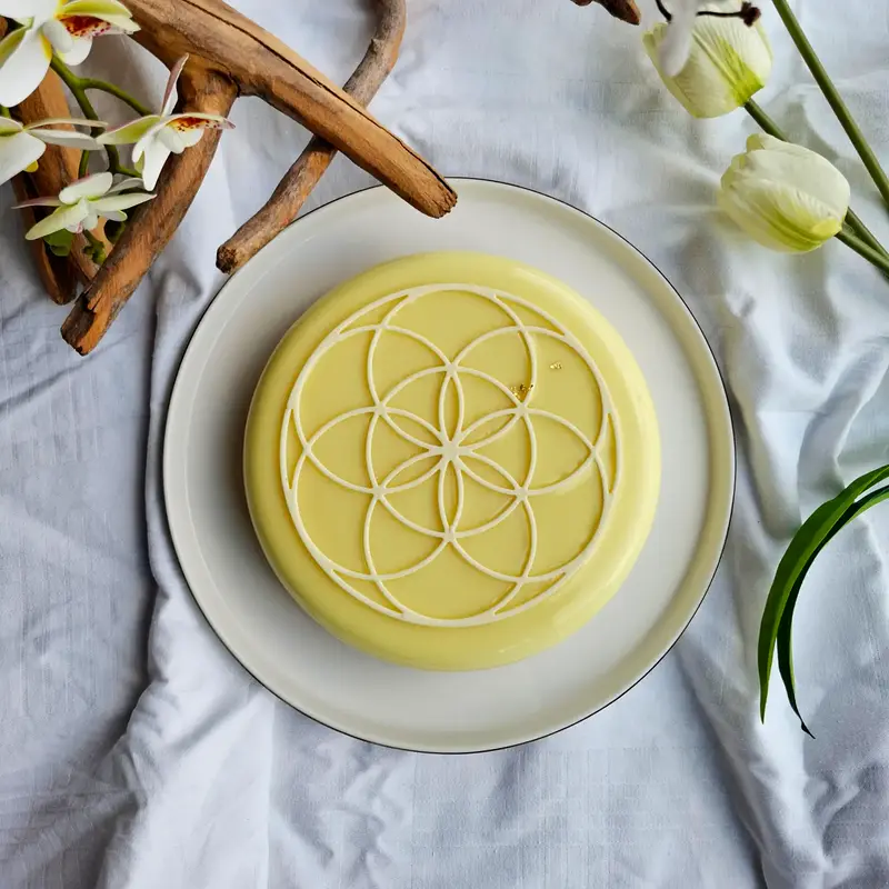 Vista dall'alto della torta Luce, con glassa giallo tenue e un decoro a cerchi intrecciati in cioccolato bianco.