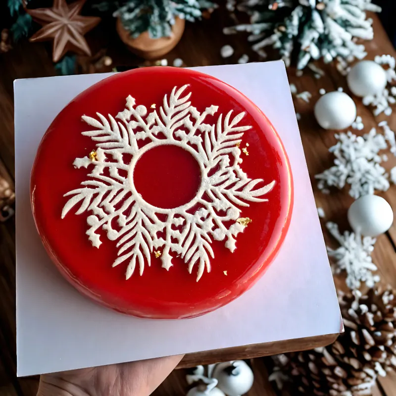 Torta semifreddo natalizia con glassa rossa a specchio, decoro bianco a fiocco di neve e foglia d'oro.