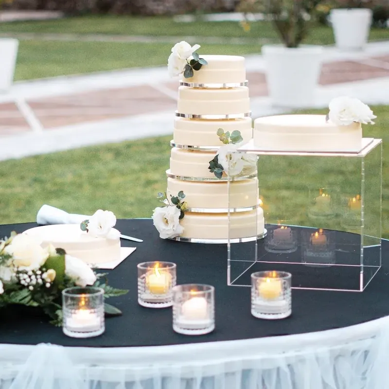 Torta nuziale bianca a sei piani con rose bianche, accanto a una seconda torta su un'alzata in plexiglass, fra candele accese.