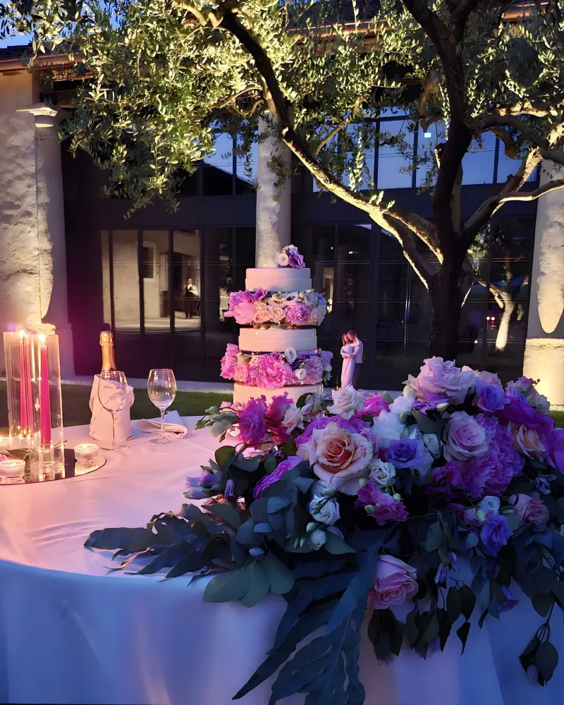 Torta nuziale a tre piani con fiori fra gli strati, allestita su un tavolo in legno con composizioni floreali.