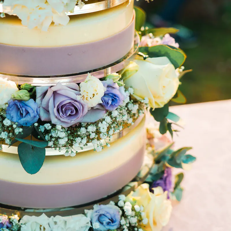 Torta nuziale a tre piani nei toni del giallo con rose e fiori d'arancio, allestita all'aperto con mignon abbinati.